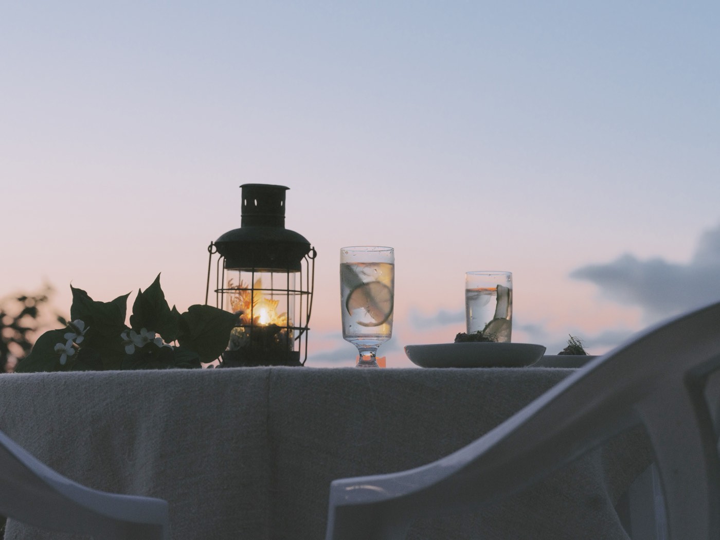 A lantern and glasses glowing on a table at dusk